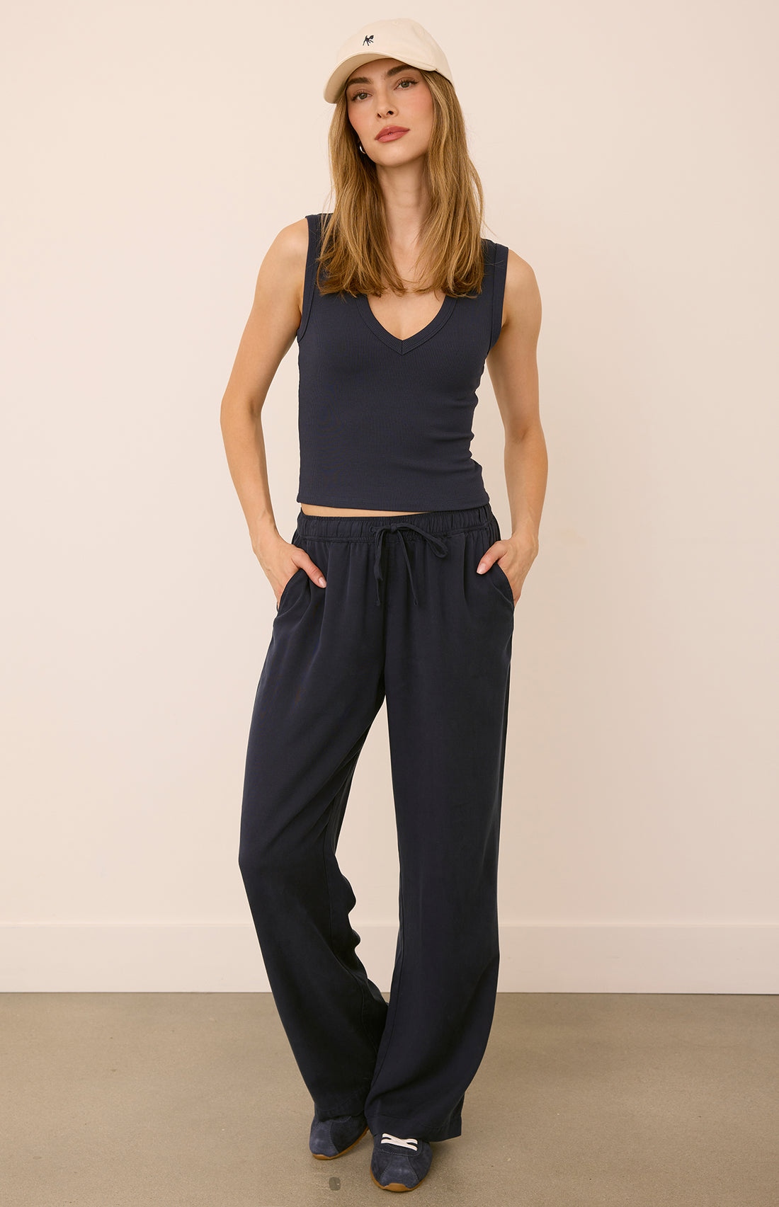 a woman in a navy tank top, navy pants and a cream hat